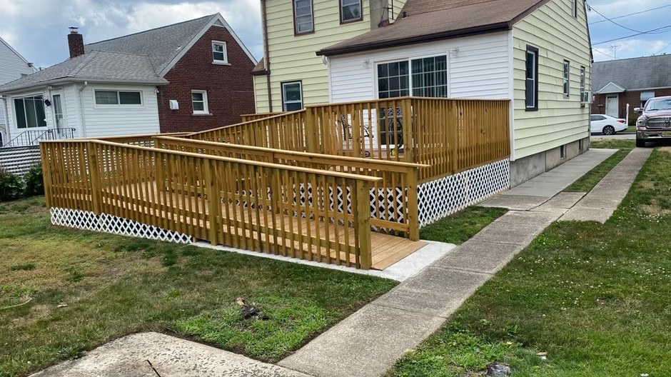 Wood exterior ramp, landing, and railings beside a home