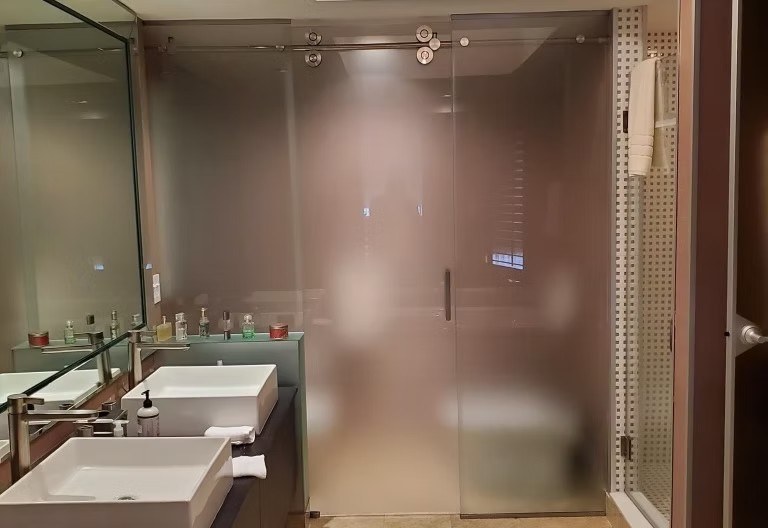 Bathroom with two vessel sinks, mirrored wall, and frosted sliding glass panel