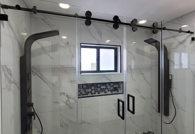 Glass-enclosed shower with black sliding-door hardware, marble-look tile, and mosaic-lined niche