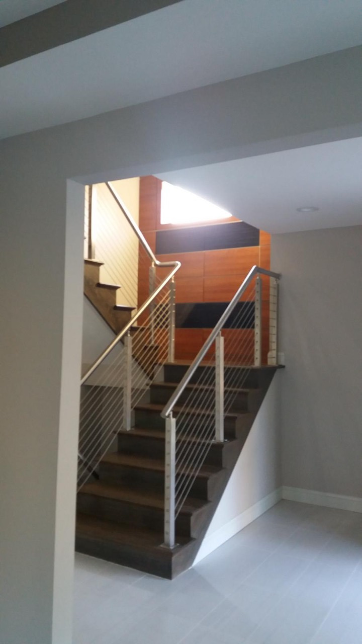 Dark wood staircase with metal posts, horizontal cable railing, and wood-paneled accent wall