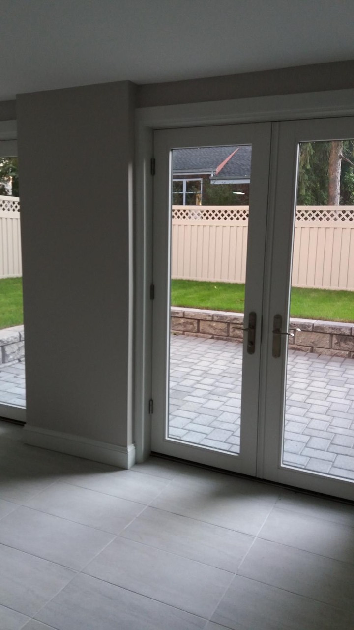 White glass double doors opening from a tiled interior to a paved backyard patio