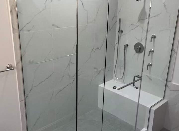 Glass-enclosed marble-look shower with built-in bench, handheld fixture, and grab bars
